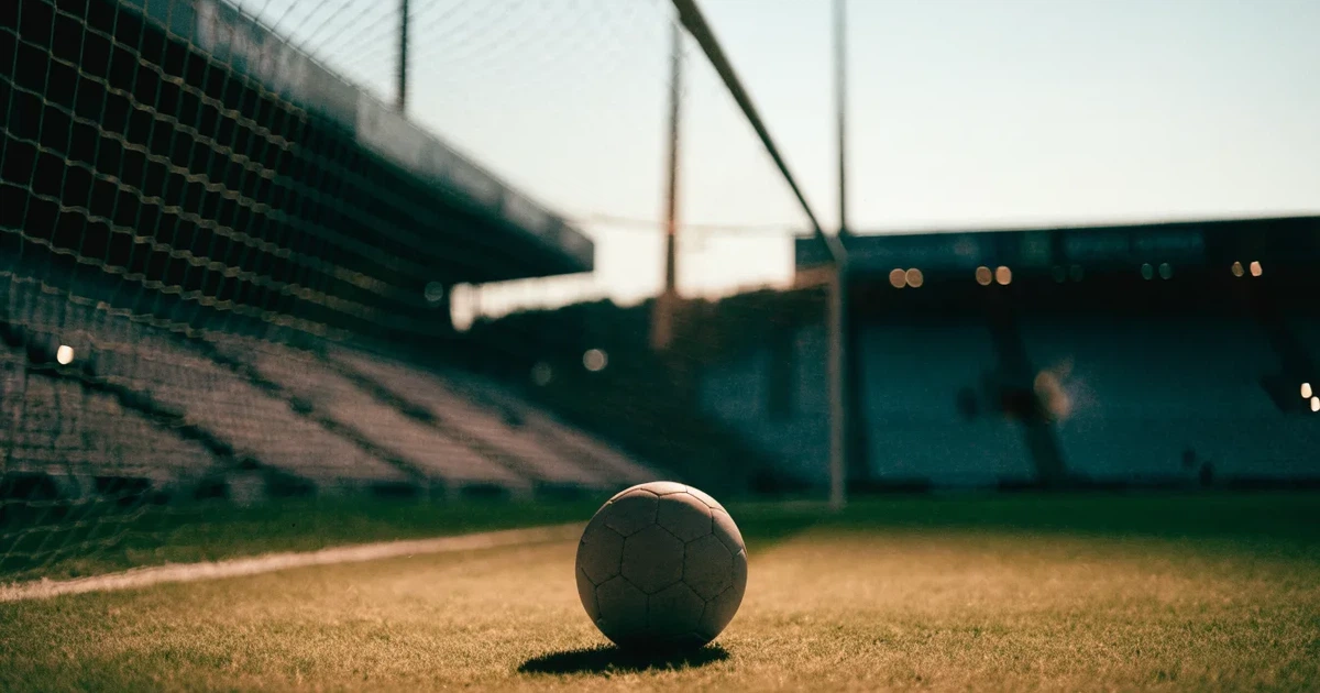 Ein Fußball liegt im Strafraum direkt vor dem Tor mit Netz, im Hintergrund leere Ränge bei Dämmerung.