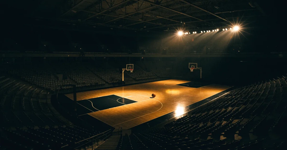 Eine leere Basketballhalle von einer oberen Tribünenreihe aus gesehen, Parkett und Körbe im Licht der Hallenstrahler.